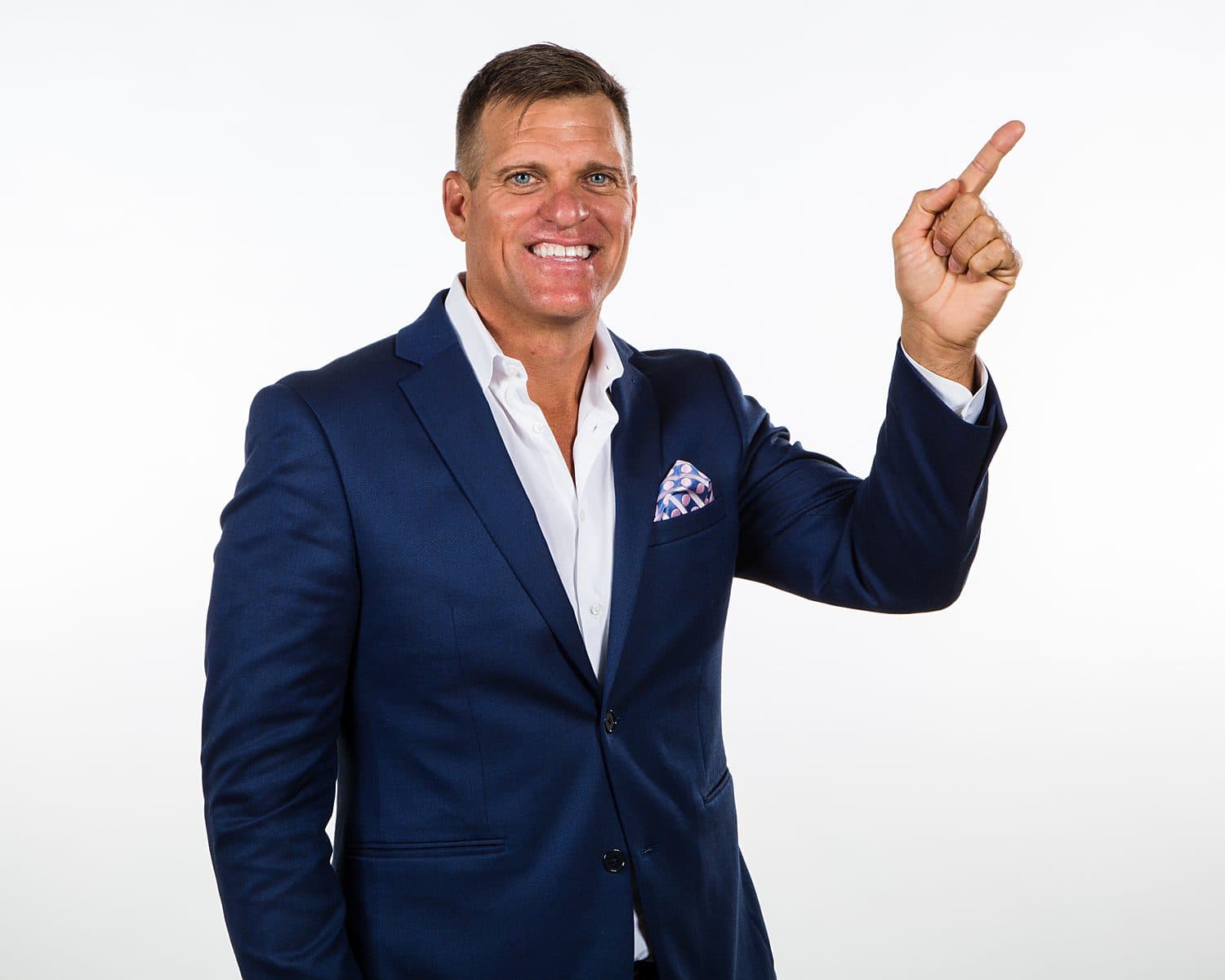 Dave VanHoose in a navy suit pointing upward: bigger stages